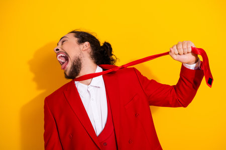 Funny bold man in red suit pulls on a bright red tie and laughs against a vivid yellow backdrop creating a playful stylish moment for fashion and entertainment mediaの写真素材