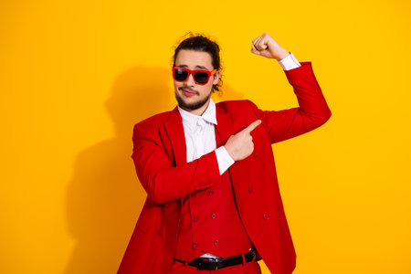 Funny stylish man in red suit posing with flexing arm against bright yellow background for fashion adの写真素材