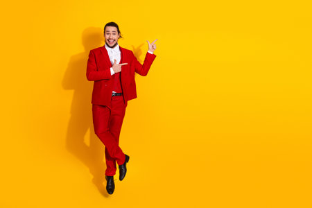 Energetic man in bold red suit leaps with joy against a bright yellow backdrop for lively fashion and holiday promotion visualsの写真素材