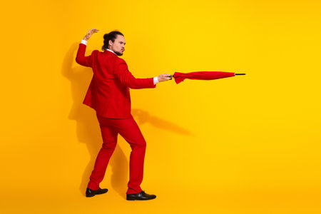 Dynamic stylish man in red suit and umbrella striking a bold pose against a bright yellow backdrop for a funny fashion momentの写真素材