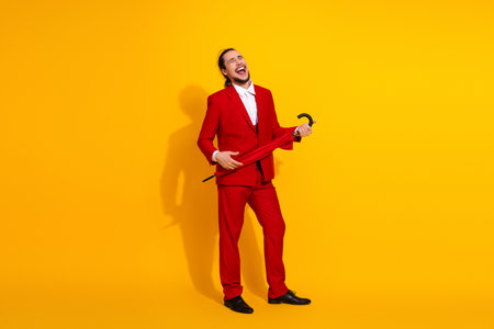 Funny stylish man in red suit laughs and twirls umbrella against bright yellow backdrop for bold fashion momentの写真素材