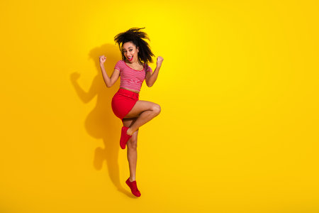 Energetic young woman striking a playful dance pose against a vibrant yellow background showcasing joy and styleの写真素材