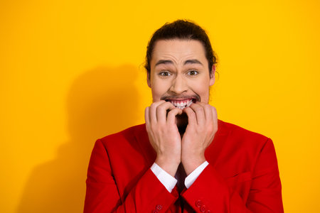 Funny man bites nails in a red suit on a bright yellow background creating a bold playful fashion promo conceptの写真素材