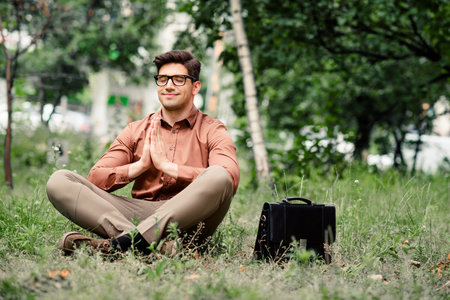 Young businessman meditating outdoors in a suit, blending work and relaxation in a serene urban park settingの写真素材