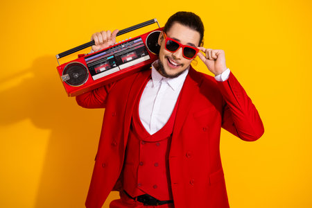 Funky red suit man with retro boombox poses confidently against a bright yellow background creating a glamorous modern party vibe and playful street styleの写真素材