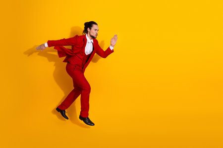 Brunet man in red suit leaps across a bold yellow background in a stylish funny active pose for fashion energy and modern promotionの写真素材