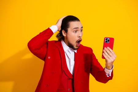 Funny fashion moment as man in red suit records reaction video on bright yellow backgroundの写真素材