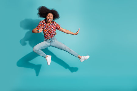 Energetic young woman leaps in the air against a blue background wearing casual fashion