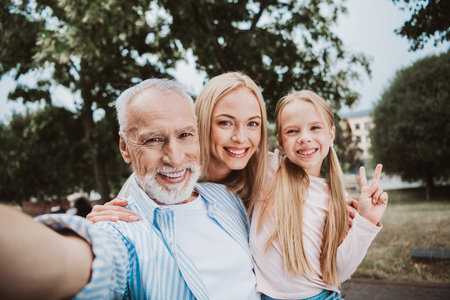 Playful grandpa daughter and granddaughter share a sunny park selfie bursting with love laughter and family bond in a lively outdoor momentの写真素材