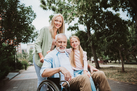 Cheerful family in the park with grandpa in a wheelchair sharing a joyful moment with his daughter and mother nearbyの写真素材
