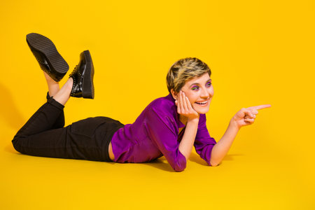Young stylish woman lying on yellow background pointing and smiling in purple blouse and black pants