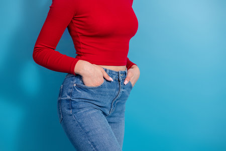 Stylish young woman wearing a red top and jeans posing against a vibrant blue background showcasing modern casual fashionの写真素材