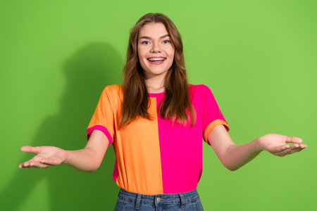 Young woman with bright color blocking shirt smiles with open arms against green background...