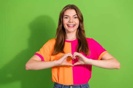 Young woman smiling in colorful outfit forms heart with hands vibrant green backdrop lifestyle...