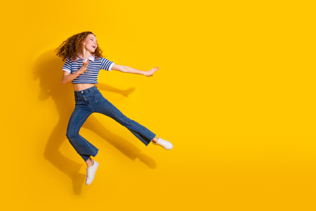 Young woman jumps with joy against a bright yellow background wearing a striped shirt and jeansの写真素材