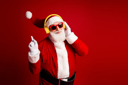 Santa wearing yellow headphones and red sunglasses in a festive red studio setting for a holiday...