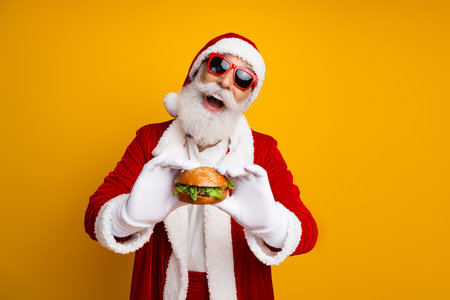 Charismatic Santa Claus in festive attire holding a delicious burger, exuding holiday spirit against a vibrant yellow winterの写真素材
