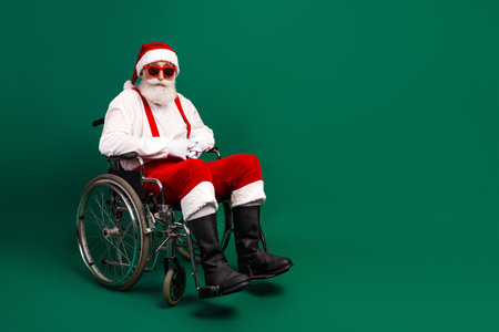 Santa Claus in Wheelchair Wearing Sunglass in Festive Attire Against a Green Background for Holiday Imageryの写真素材