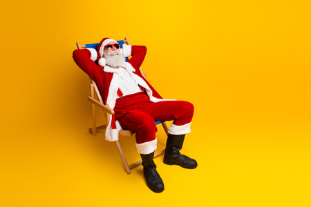 Cheerful Santa Claus relaxing in a deck chair against a vibrant yellow background, enjoying a fun and festive holiday momentの写真素材