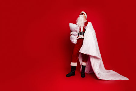 Santa in red suit with pillow and blanket against red background ready for holiday fun and festive poseの写真素材
