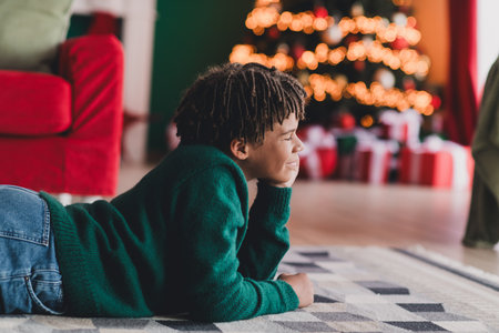Young boy enjoying the cozy holiday atmosphere near a Christmas tree with colorful decorations and festive lightsの写真素材