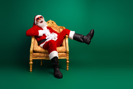 Santa Claus sitting stylishly in a gold armchair wearing cool sunglass against a vibrant green backgroundの写真素材