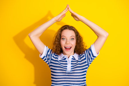 Young woman with curly red hair in a striped shirt celebrates with hands raised above her head...