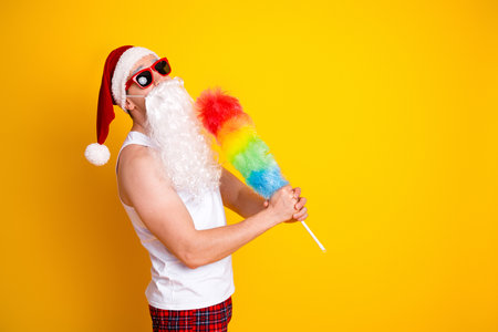 Santa character with rainbow feather duster poses in a bright yellow background for festive fun and holiday humor in a playful home sceneの写真素材