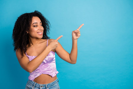 Young girl wearing a lilac top smiles and points to the right against a vivid blue background for fashion lifestyle and beauty campaignsの写真素材