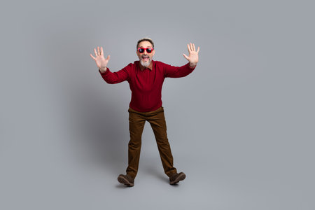 Mature male in casual red sweater with stylish sunglass gesturing on a gray background, exuding confidence and energyの写真素材
