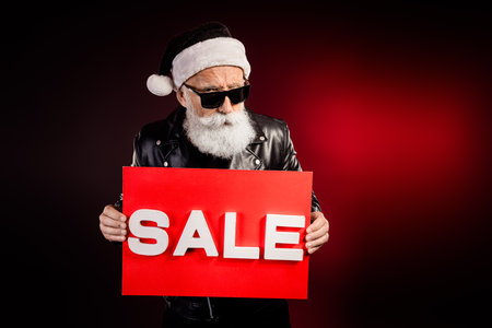 Santa rocker in leather jacket holds a bold red sale sign in a moody Christmas studio scene perfect for festive marketing and holiday shopping campaignsの写真素材