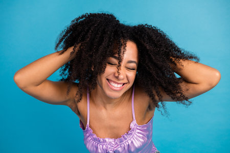 Playful young woman with curly hair laughs and tosses her head against a blue background in a bright casual fashion portraitの写真素材
