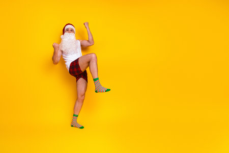 Joyful Santa look alike in pajama shorts striped socks leaps against yellow background festive energy and humor for Christmas campaignsの写真素材