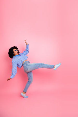 Stylish young woman in casual attire making a funny pose against a vibrant pink background showcasing expressive energyの写真素材