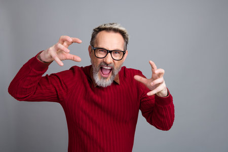 Energetic mature businessman gesturing dynamically while showcasing confidence in a red sweater against a clean gray backdropの写真素材