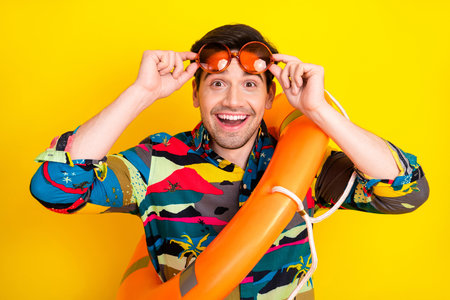 Young man with colorful shirt and orange lifebuoy poses against a yellow background smiling for a...