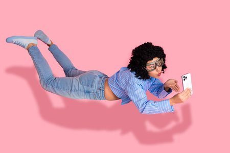 Cheerful young woman with curly hair taking a selfie against a vibrant pink background in casual outfitの写真素材