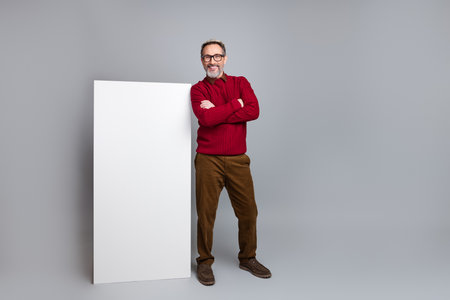 Confident senior businessman in casual attire standing next to a white board against a modern gray backgroundの写真素材