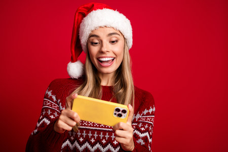 Funny shopper in a Santa hat texts on a yellow phone and smiles brightly for a holiday moment during winter season with a red sweater vibeの写真素材