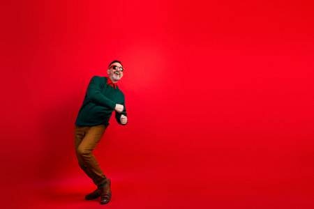 Fun energetic man in green sweater dances against red backdrop perfect for holiday season and Christmas themed stock photographyの写真素材