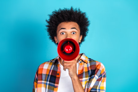 Young man with megaphone on bright blue background expressing energy style and mood in casual plaid shirtの写真素材