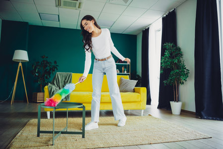 Young woman cleaning at home in a bright modern living room with a colorful duster creating a...