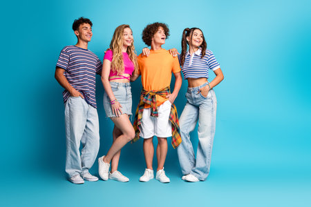 Playful group of four teens posing with energy and style as friends celebrate summer vibes against a bright blue studio backdropの写真素材