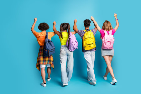 A playful group of four students with colorful backpacks celebrate friendship against a bright blue backdropの写真素材