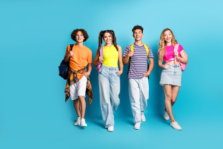Four trendy teens pose with bright backpacks and casual outfits against a vivid blue studio background for a fun friendship themed stock imageの写真素材