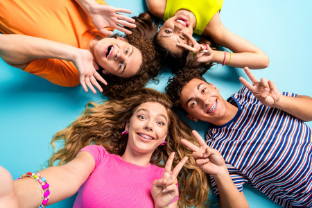 fun loving friends circle selfie colorful group of teens lying on blue background showing peace...