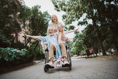 Fun sunny family park moment with grandpa in wheelchair daughter and mother sharing joy and resilience togetherの写真素材