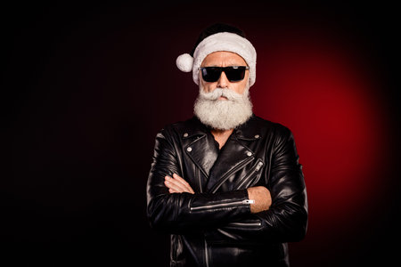 Santa rocker in leather jacket with white beard black sunglass stands confidently in festive studio embodying modern holiday cool Christmas spiritの写真素材