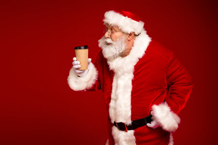 Santa in a red suit with coffee cup exudes festive cheer against bold red backdrop perfect for Christmas ads and holiday campaignsの写真素材