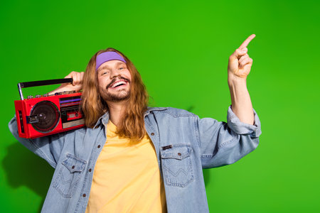Young stylish man in retro outfit pointing and holding boom box against green background, expressing joy and energyの写真素材